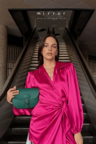 Woman in a fuchsia dress with a green bag on an escalator, Mirror campaign, fashion
