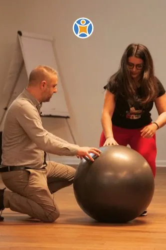 Two people doing a posture exercise with a ball, Postura Facile campaign